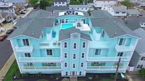 Uma casa grande, azul clara, com vários andares, piscina, várias varandas e uma entrada central.