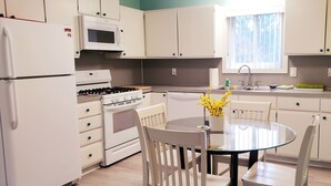 A modern kitchen with white appliances, a round glass table, and chairs.