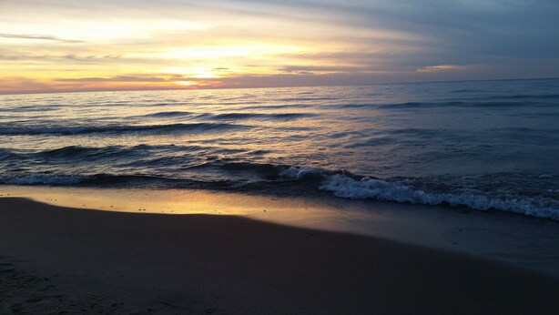 A beach with waves and a sunset.