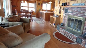 A cozy living room with a fireplace, wooden furniture, and a kitchen area with a telephone sign. - Lake Winnipesaukee Waterfront! Family Friendly, Amazing View, HotTub,Kayaks+more (Alton Bay)