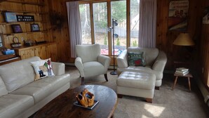 A cozy living room with a wooden interior, featuring two sofas, a coffee table, and a side table with books. - Lake Winnipesaukee Waterfront! Family Friendly, Amazing View, HotTub,Kayaks+more (Alton Bay)