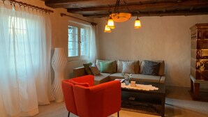 A cozy living room with a wooden ceiling, a sofa with cushions, a red armchair, and a table with a vase. - Superior Family Apartment in old house  built in 1707 (Laufen-Uhwiesen)