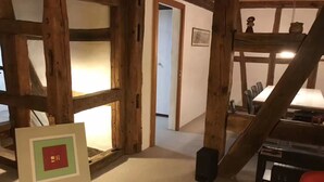 A room with exposed wooden beams, a framed picture on the floor, a table with items, and a door leading to another room. - Superior Family Apartment in old house  built in 1707 (Laufen-Uhwiesen)