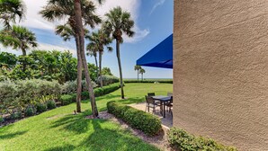 A patio area with a table and chairs, surrounded by palm trees and well-maintained hedges. - Unit #120 Sand Cay Beach Resort Gulf View (Longboat Key)