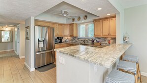 A modern kitchen with wooden cabinets, stainless steel appliances, a marble countertop, and a ceiling fan. - Unit #120 Sand Cay Beach Resort Gulf View (Longboat Key)