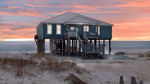 A beachfront house with a deck and stairs leading to the entrance.