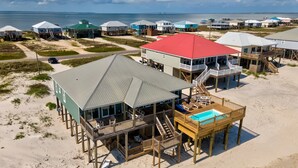 A beachfront property with multiple wooden structures, including a main building with a red roof and a separate pool area.