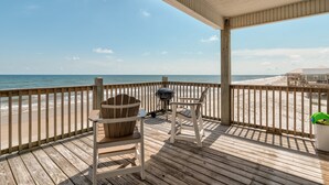 A wooden deck with two Adirondack chairs, a grill, and a view of the beach.