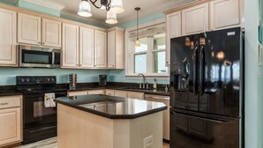 A modern kitchen with light-colored cabinets, a black refrigerator, a microwave, and a stove.