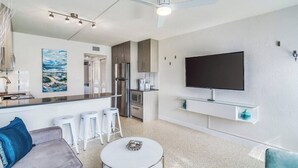 A modern kitchen with a built-in oven, a refrigerator, and a microwave. There is a dining area with a white table and chairs. A flat-screen TV is mounted on the wall. - Fabulous 1br New Coastal Apt Steps to the Beach! - Unit D (Cocoa Beach)