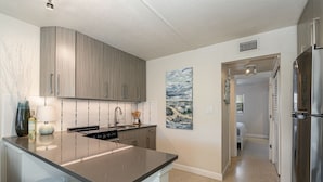 A modern kitchen with a curved island, stainless steel appliances, and a painting on the wall. - Fabulous 1br New Coastal Apt Steps to the Beach! - Unit D (Cocoa Beach)