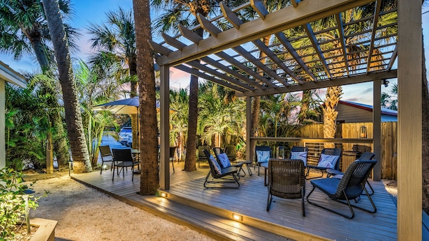 A covered outdoor seating area with wooden deck, lounge chairs, and a pergola structure. - Fabulous 1br New Coastal Apt Steps to the Beach! - Unit D (Cocoa Beach)