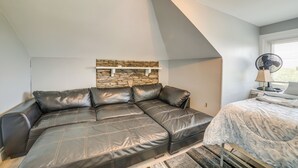 A modern loft bedroom with a sectional sofa, a stone accent wall, a bed with a patterned bedspread, and a standing fan. - Pittsburgh Vacation Rental ~ 6 Mi to Downtown! (Pittsburgh)