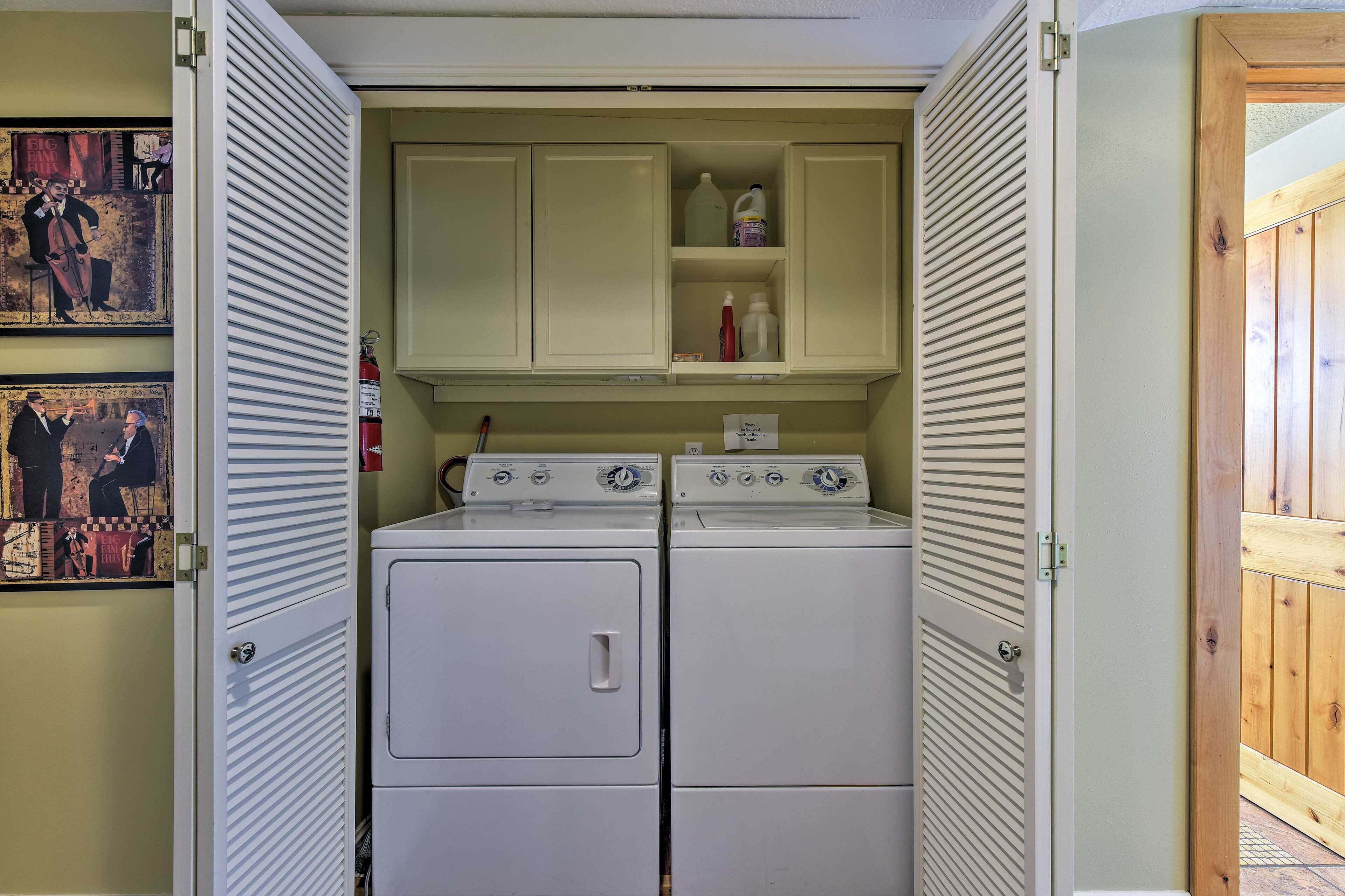 A laundry room with two stacked washers and dryers, a shelf with cleaning supplies, and artwork on the walls.