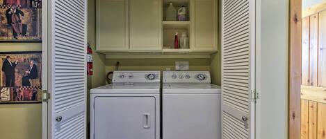 A laundry room with two stacked washers and dryers, a shelf with cleaning supplies, and artwork on the walls.