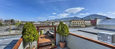 A rooftop deck with potted plants, a pergola, and a view of a cityscape and mountains.