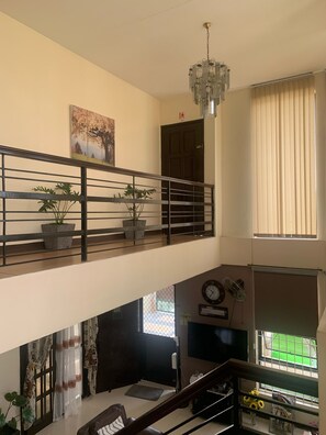 Ein mehrstöckiger Wohnbereich mit Treppe, Topfpflanzen, einem Chandelier und einem Fernseher.