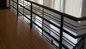 Ein geräumiges Zimmer mit Holzboden, schwarzer Geländer und großen Fenstern mit Jalousien.