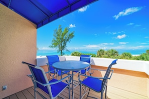 A covered outdoor seating area with a table and chairs, overlooking a beach and ocean. - Unit #302 Sand Cay Beach Resort Gulf Front (Longboat Key)
