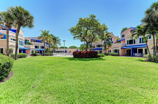 A hotel courtyard with a well-maintained lawn, palm trees, and a central flower bed. - Unit #113 Sand Cay Beach Resort Pool View (Longboat Key)
