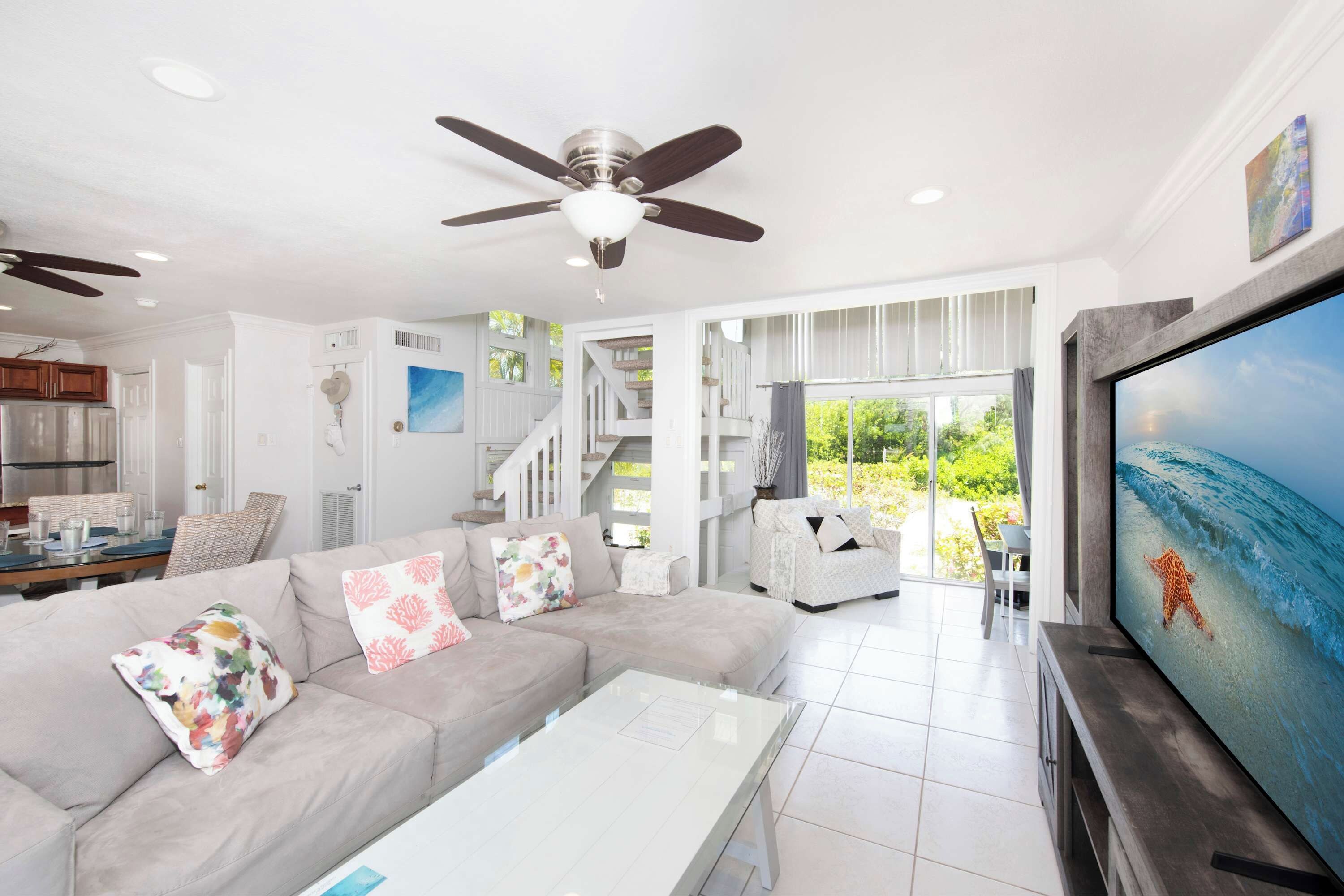 Un salon moderne doté d’un grand téléviseur à écran plat, d’un ventilateur de plafond et d’un escalier menant à un espace extérieur.