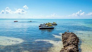 Klares blaues Meer mit Jetskis und einem Felsen.