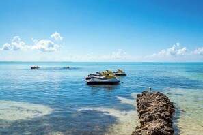 Mar azul cristalina con motos acuáticas y un promontorio rocoso.