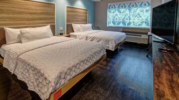 A hotel room with two beds, a large window with a geometric pattern, a flat-screen TV, and a wooden floor.