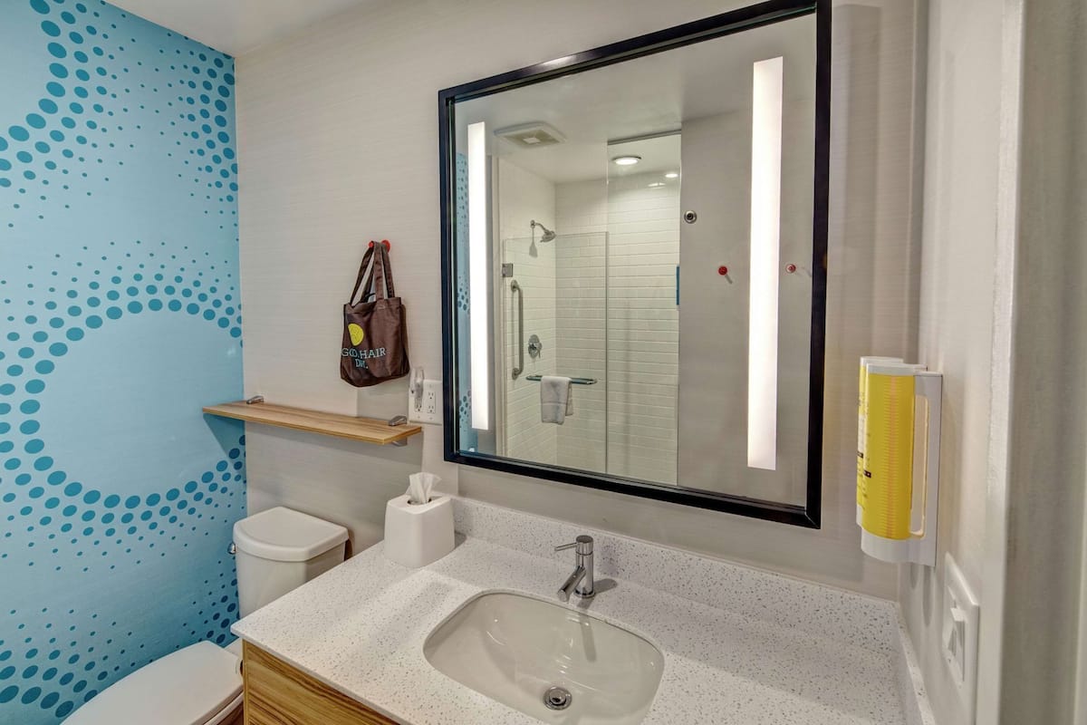 Ein Badezimmer mit einer weißen Toilette, einem Waschbecken mit Spiegel darüber, einem Handtuchhalter und einer Wand mit blauem Punktmuster.
