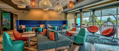 Un espacio lounge moderno con un sofá modular, sillas turquesa y naranja, y sillones colgantes.