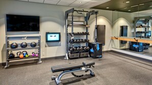 Ein Fitnessraum mit einer Bank, Kettlebells, Kurzhanteln und einem Fernsehbildschirm.