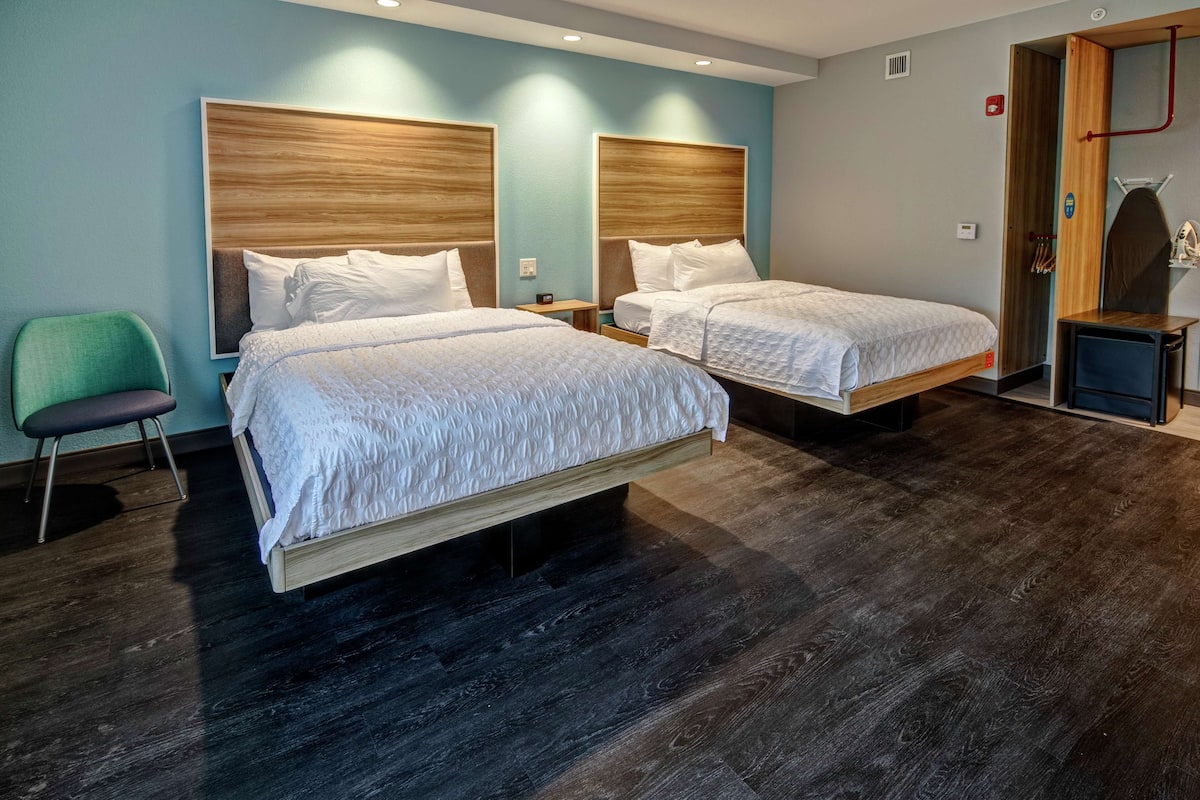 Ein Hotelzimmer mit zwei Betten, einem grünen Sessel und Holzboden.