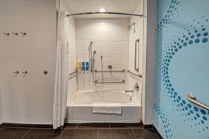 Un baño moderno con ducha a ras de suelo, paredes de azulejos blancos, una bañera con una toalla y un papel tapiz azul con estampado.