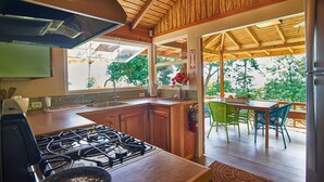 A kitchen with wooden cabinets, a gas stove, and a window overlooking a patio with chairs and a table. - Eagle's Base Villa & Cottage (Scarborough)