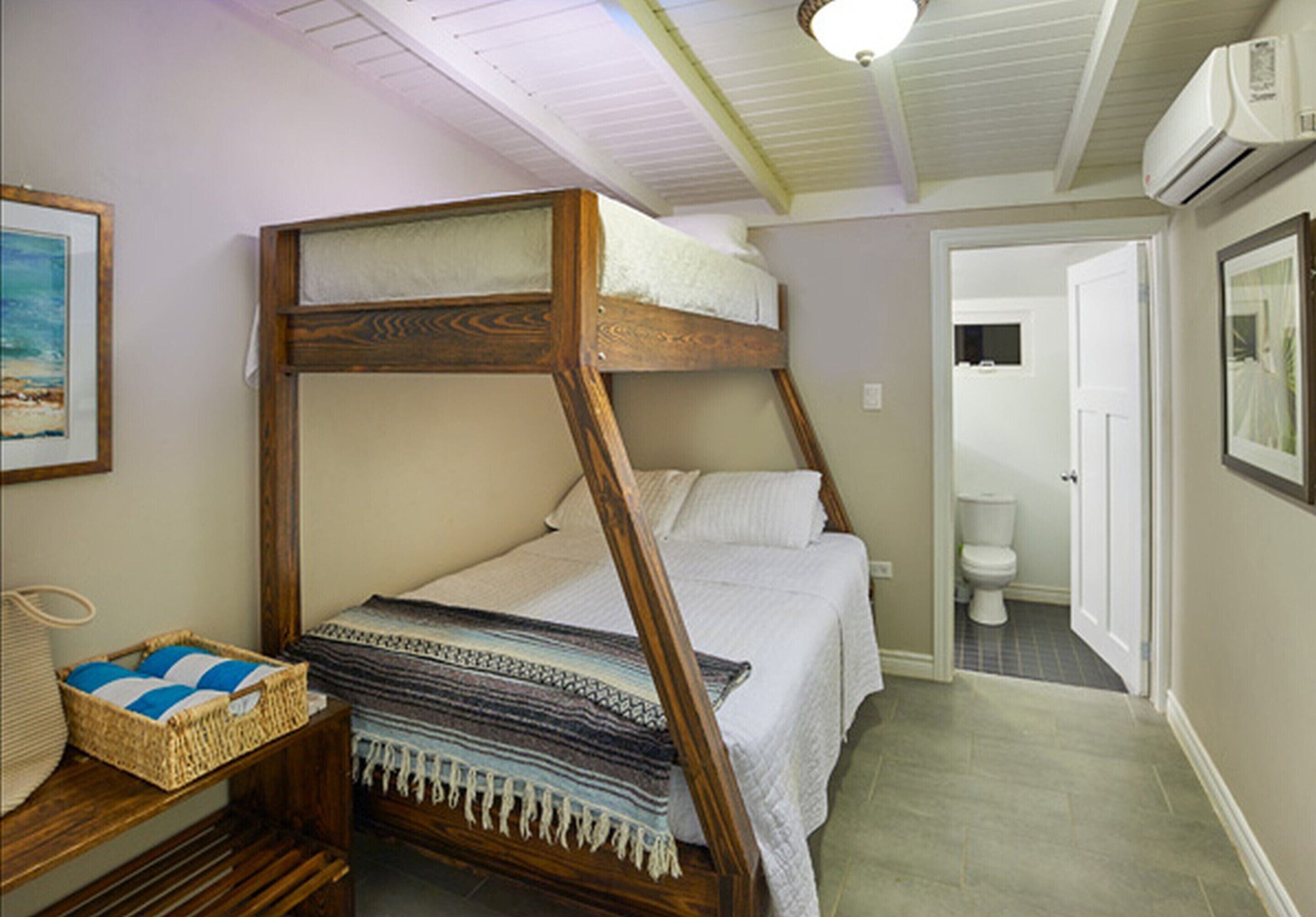 A single bedroom with a wooden bunk bed, a bedside table with a basket, and a door leading to a bathroom.