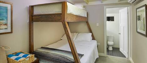 A single bedroom with a wooden bunk bed, a bedside table with a basket, and a door leading to a bathroom.