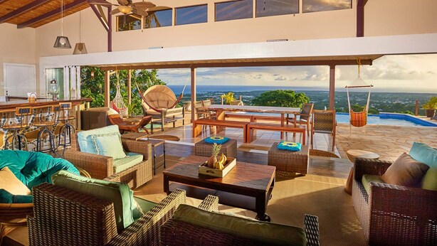 A spacious outdoor lounge area with wicker furniture, ceiling fans, and a view of the ocean. - Eagle's Base Villa & Cottage (Scarborough)