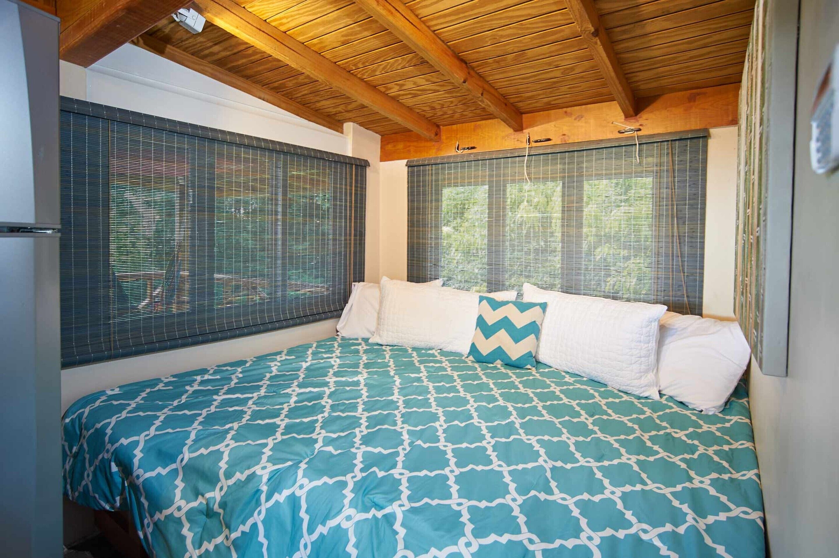 Un dormitorio con cama, ventanas amplias y vigas de madera en el techo.