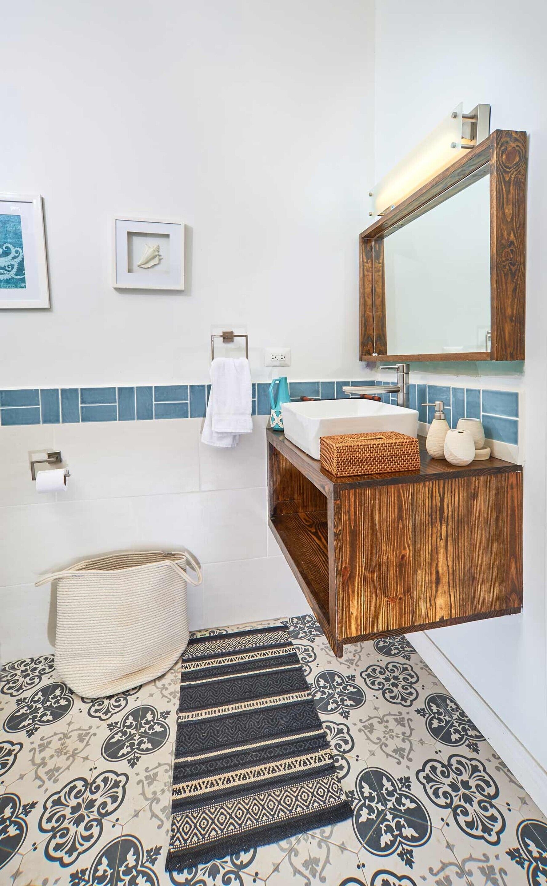 A bathroom with a wooden vanity, a large mirror, a bathtub, and patterned tiles.