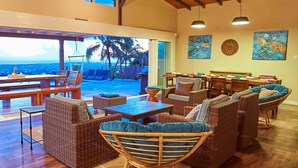 A spacious lounge area with wicker furniture, a pool view, and wooden beams on the ceiling. - Eagle's Base Villa & Cottage (Scarborough)