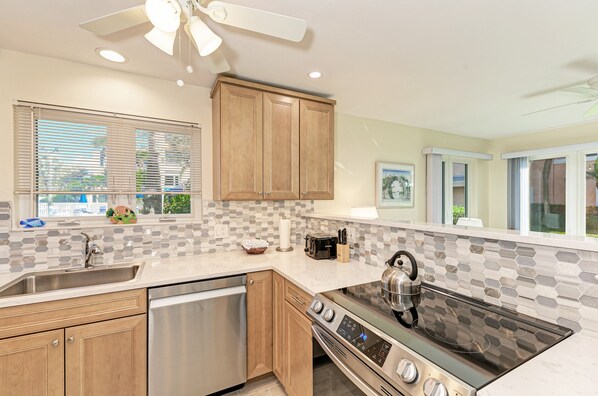 A modern kitchen with a dishwasher, stove, and wooden cabinets. - Unit #106 Sand Cay Beach Resort Gulf View (Longboat Key)
