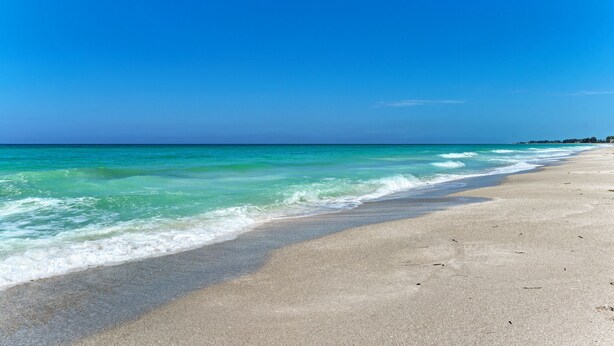 Une plage aux eaux turquoise et limpides, bordée d’un rivage sablonneux.