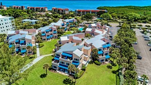 An aerial view of a resort with multiple buildings, a parking area, and a view of the ocean. - Unit #103 Sand Cay Beach Resort Gulf Front (Longboat Key)