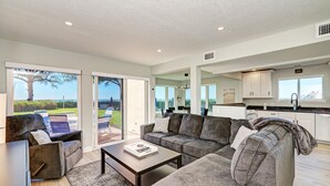 A modern living room with a sectional sofa, a coffee table, and a view of the outdoors. - Unit #103 Sand Cay Beach Resort Gulf Front (Longboat Key)