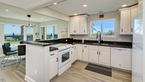 A modern kitchen with white cabinetry, a built-in oven, and a large island with a sink. - Unit #103 Sand Cay Beach Resort Gulf Front (Longboat Key)