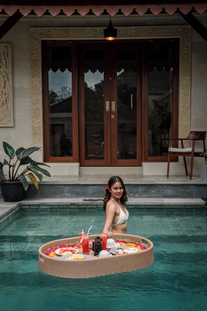 A woman standing by a pool with a floating basket containing food and drinks. - Sari Bamboo Bungalows (Ubud)