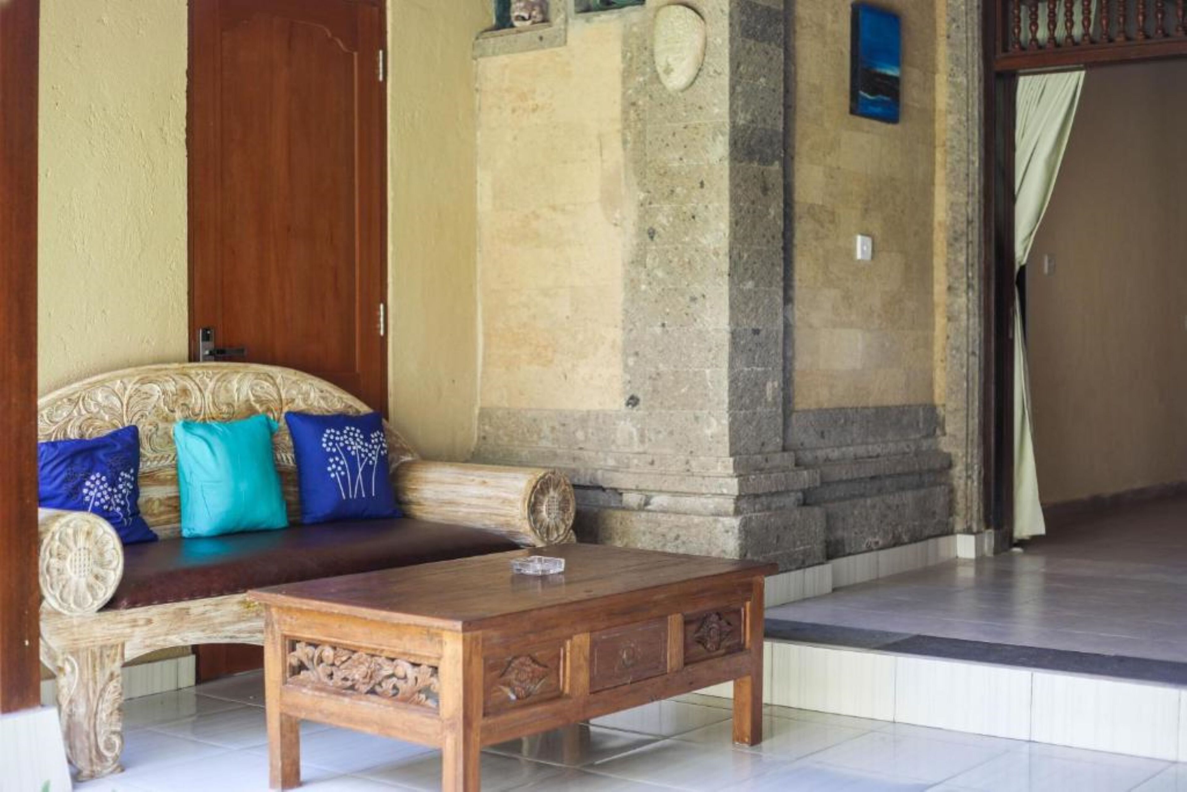A room with a wooden sofa, a coffee table, and a stone wall.
