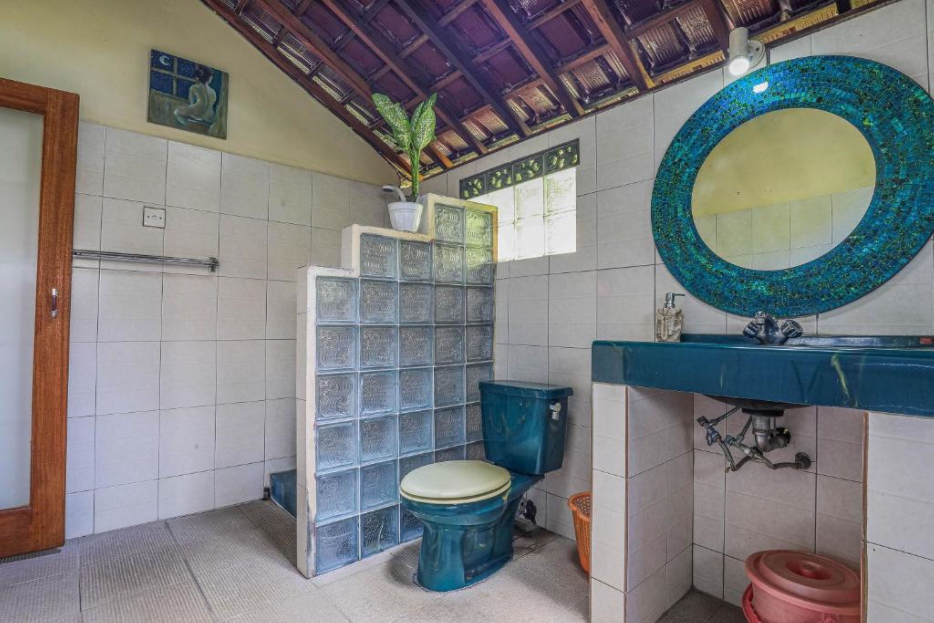 A bathroom with a blue toilet, a sink with a blue countertop, a mirror, and a potted plant.