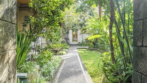A pathway flanked by lush greenery and stone walls, leading to a traditional gate. - Sari Bamboo Bungalows (Ubud)