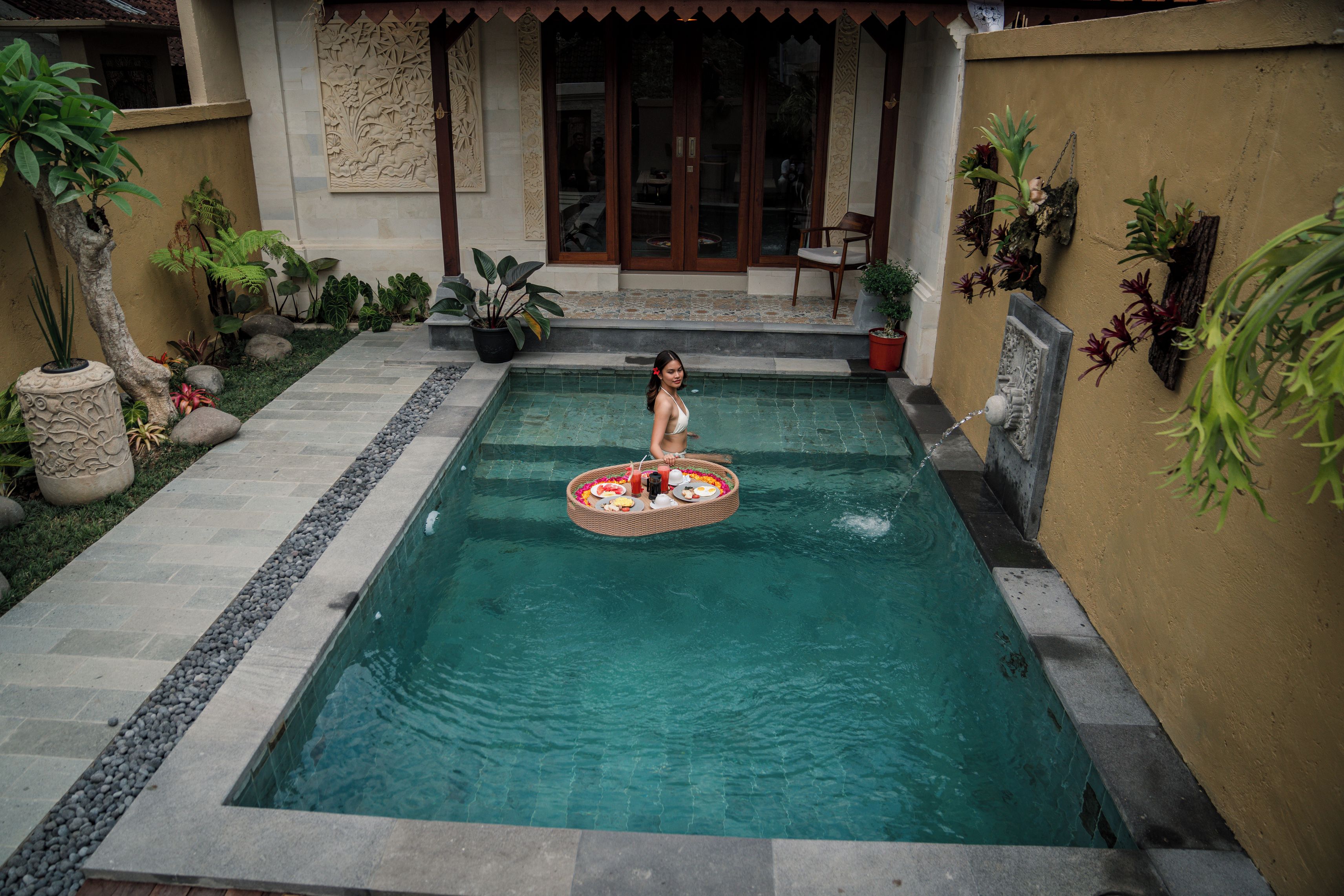 A pool with a floating tray, surrounded by potted plants and a stone pathway.